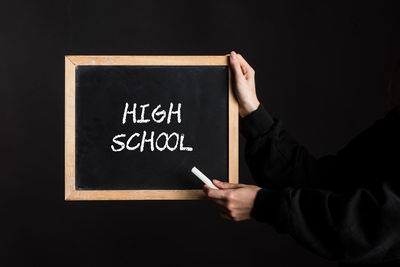 Cropped hand of person holding blackboard against black background