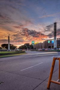 Road by illuminated buildings against sky during sunset