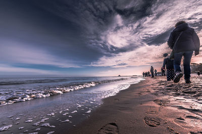 People on beach against sky during sunset