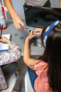 Female teacher helping girl student to assemble electrical circuit in robotics class