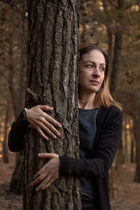 Portrait of woman standing by tree trunk in forest