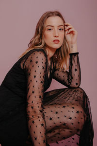 Portrait of young woman sitting against pink background