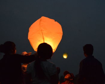 Rear view of people standing against illuminated orange sky