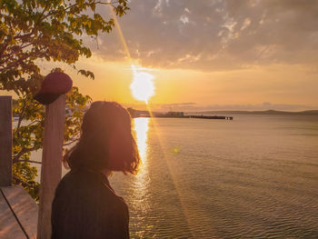 Woman standing on shore against sky during sunset