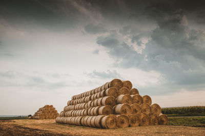 Stack of hay bales on field against sky