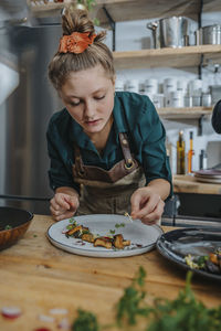 Young female chef garnishing dish while standing in kitchen