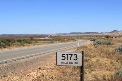 Road leading towards mountains against clear blue sky