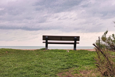 Empty bench on field against sky