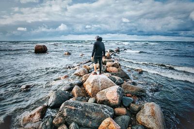 Rear view of man standing on rock against sea