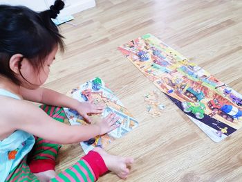 High angle view of cute girl playing with puzzles while sitting on hardwood floor at home