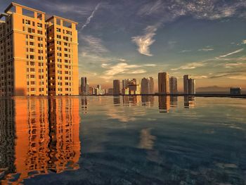 Modern buildings by sea against sky during sunset