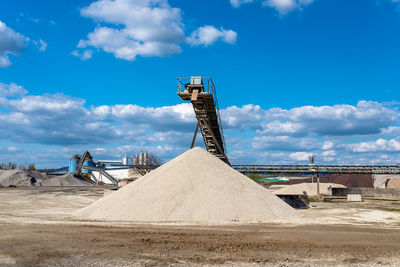 Conveyor over heaps of gravel on blue sky at an industrial cement plant.