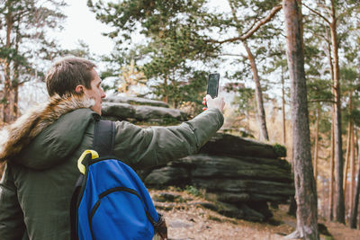 Rear view of man photographing through camera in forest