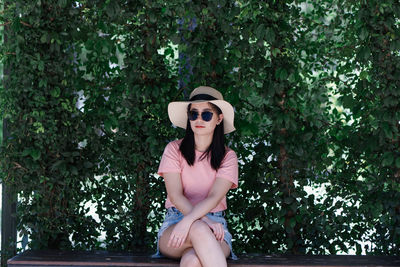 Young woman wearing sunglasses sitting on plant against trees