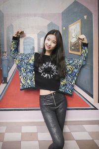 Portrait of smiling young woman standing against wall