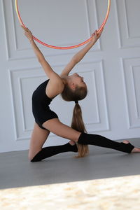 Little gymnast in a black suit doing stretching with hoop