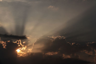 Low angle view of sunbeams streaming through clouds during sunset