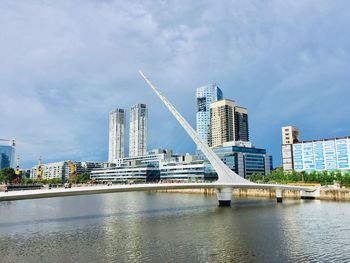 Bridge over river by buildings against sky