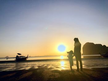 Silhouette people on beach against sky during sunset