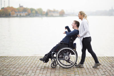 Caretaker pushing disabled man on wheelchair along lake