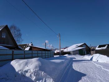 Snow covered houses by buildings against clear blue sky