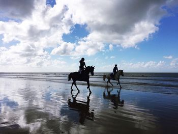 Silhouette people riding on beach against sky