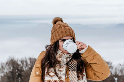 Front view of young woman drinking hot tea outdoors in winter.