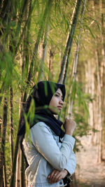 Side view of woman standing against bamboos