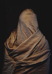 Person covered with fabric standing against black background