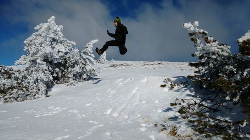 Low angle view of man jumping on snow against sky