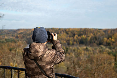 Back view of young photographer takes pictures of autumn landscape, closeup