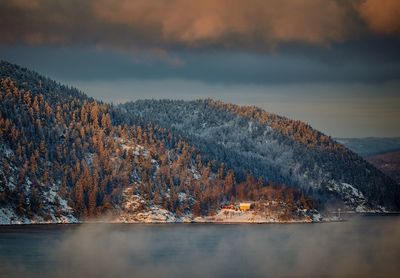 Scenic view of lake by mountains against cloudy sky during sunset