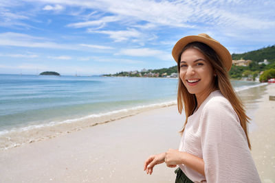 Portrait of young woman standing at beach against sky