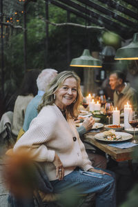 Side view portrait of smiling senior woman sitting on chair during dinner party