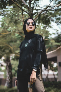 Portrait of young woman standing against trees