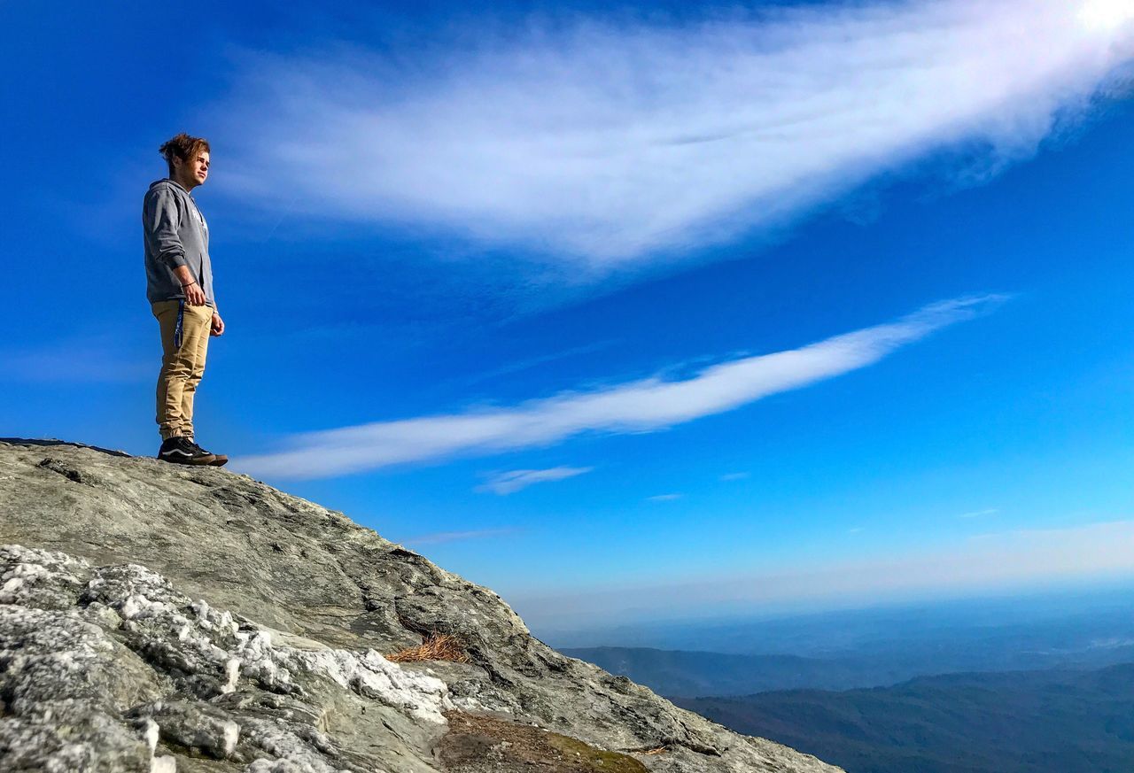 MAN STANDING ON CLIFF AGAINST BLUE SKY