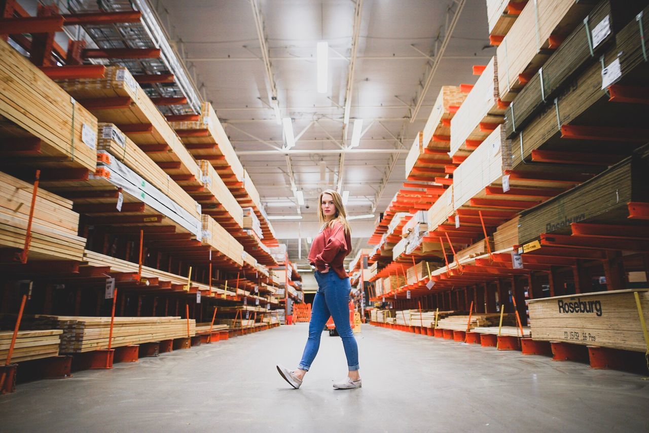 full length, real people, one person, indoors, casual clothing, looking at camera, shelf, lifestyles, warehouse, young women, standing, young adult, working, day, adult, people