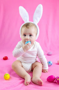 Surprised baby girl with easter egg toy sitting on pink towel at home