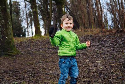 A young boy in winter clothes plays with a stick in the woods