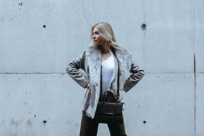 Young woman looking away while standing against wall