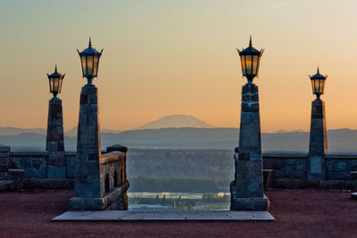 Electric lamps on retaining wall against sky during sunset