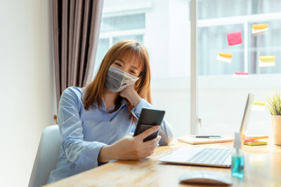 Young woman using phone while sitting on table