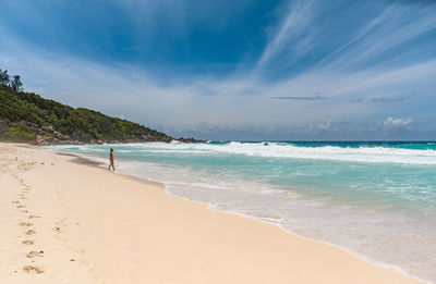 Woman standing alone on tropical sandy beach with idyllic turquoise ocean and waves