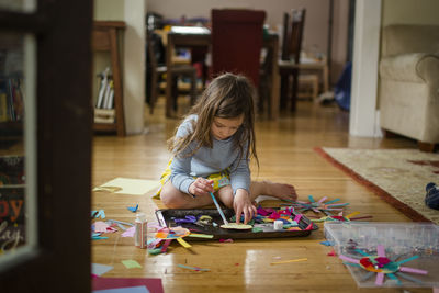 Looking through doorway at little girl sitting on floor crafting paper
