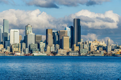 Architecture of the seattle skyline with elliott bay in front and clouds above.  and a ferry.