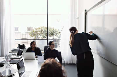 Female colleagues concentrating at businesswoman explaining diagram on whiteboard during meeting in board room