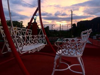 Chairs by sea against sky during sunset