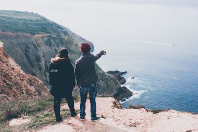 Rear view of couple standing on rock by sea