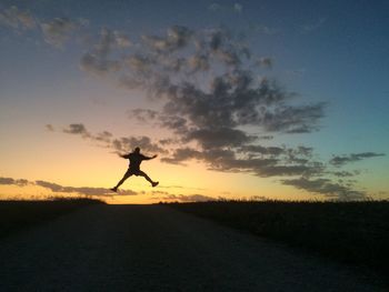 Silhouette woman jumping on landscape against sky during sunset