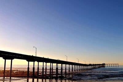 Silhouette bridge over sea against clear sky during sunset